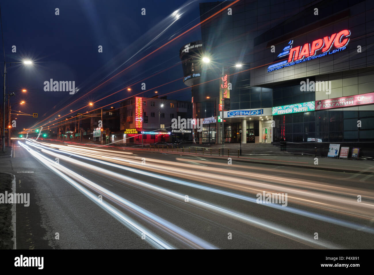 Night view of blurred traces of automobile headlights driving on central city road and building of shopping, entertainment center Sail Stock Photo