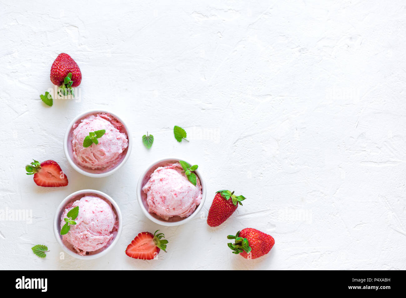Strawberry ice cream and fresh strawberries on white background, top view. Three bowls of strawberry ice cream, healthy summer dessert. Stock Photo