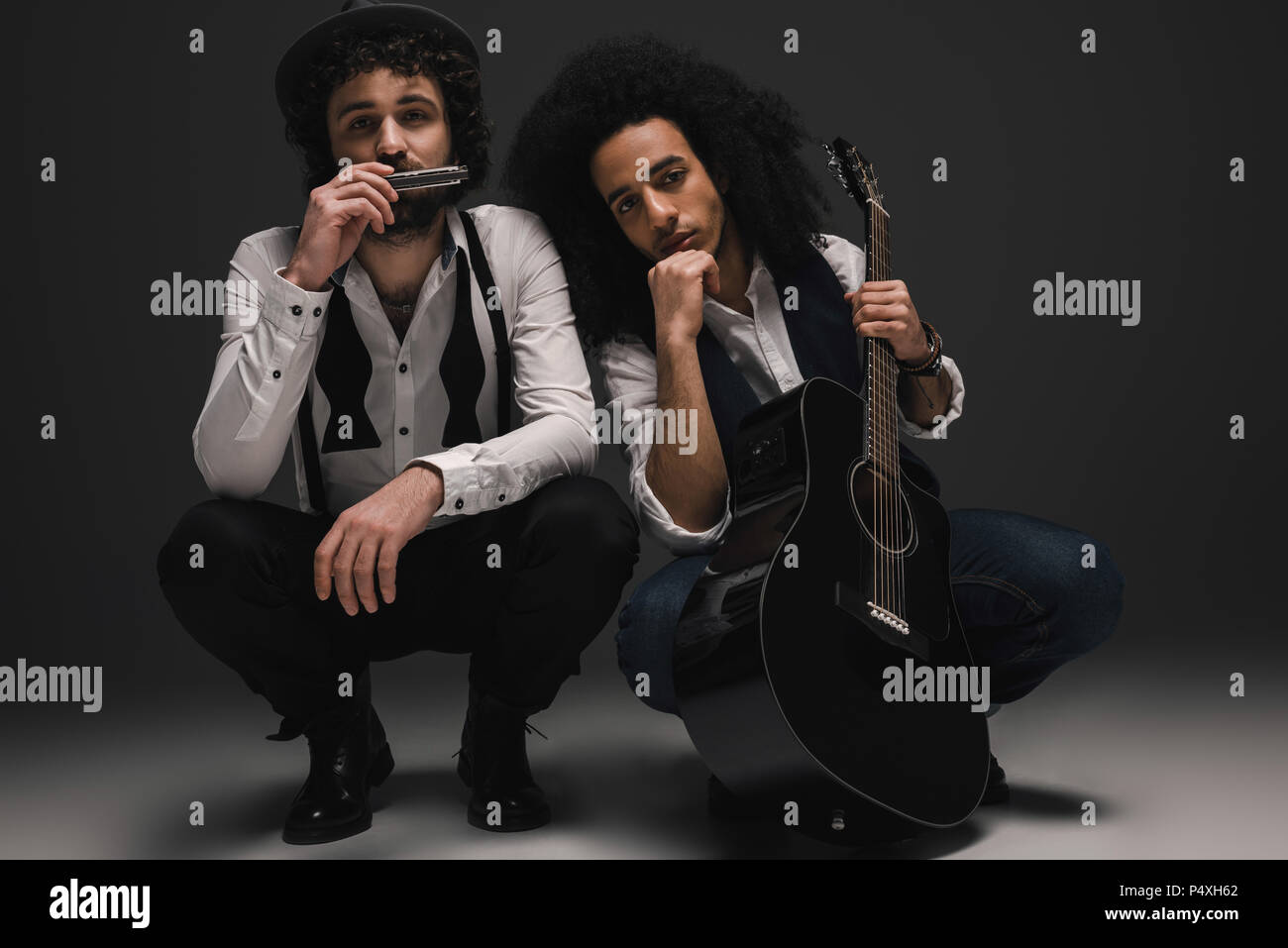 duet of musicians with guitar and harmonica sitting squat Stock Photo