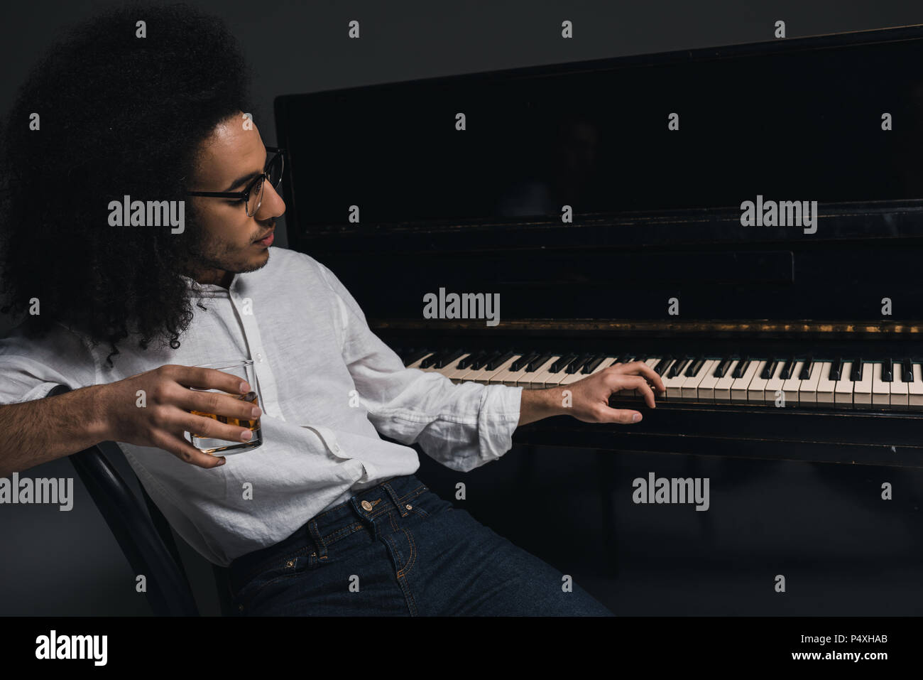handsome young musician drinking whiskey and playing piano on black