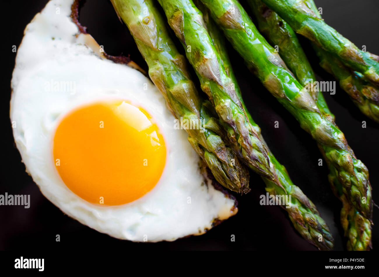 Fried egg and roasted fresh asparagus in black plate. Healthy lunch