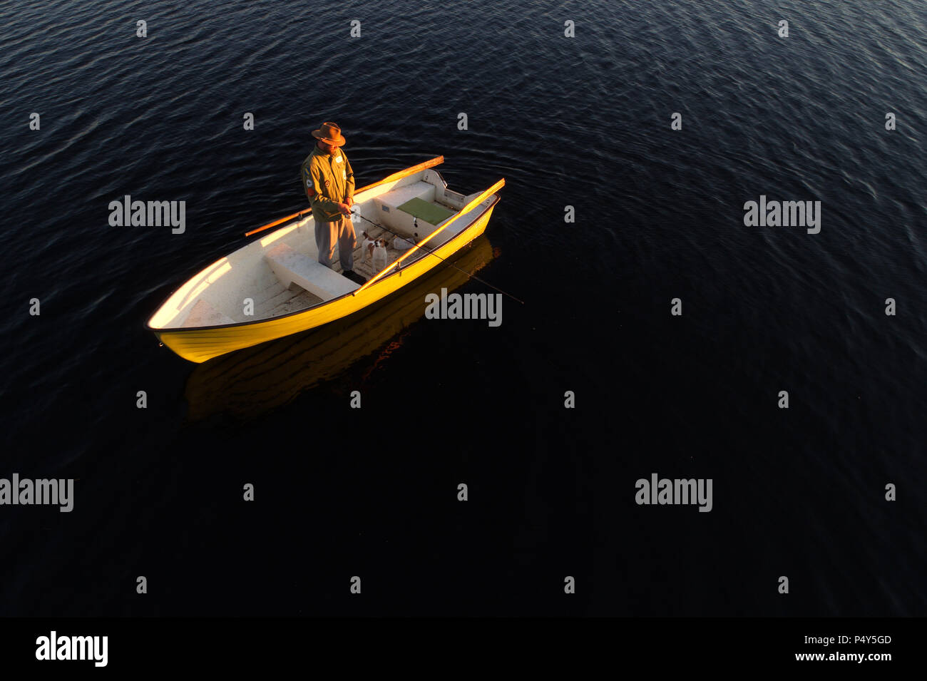 Lulea, Sweden - June 16, 2018: A man and his dog standing in a rowing boat fishing at sunset. Stock Photo