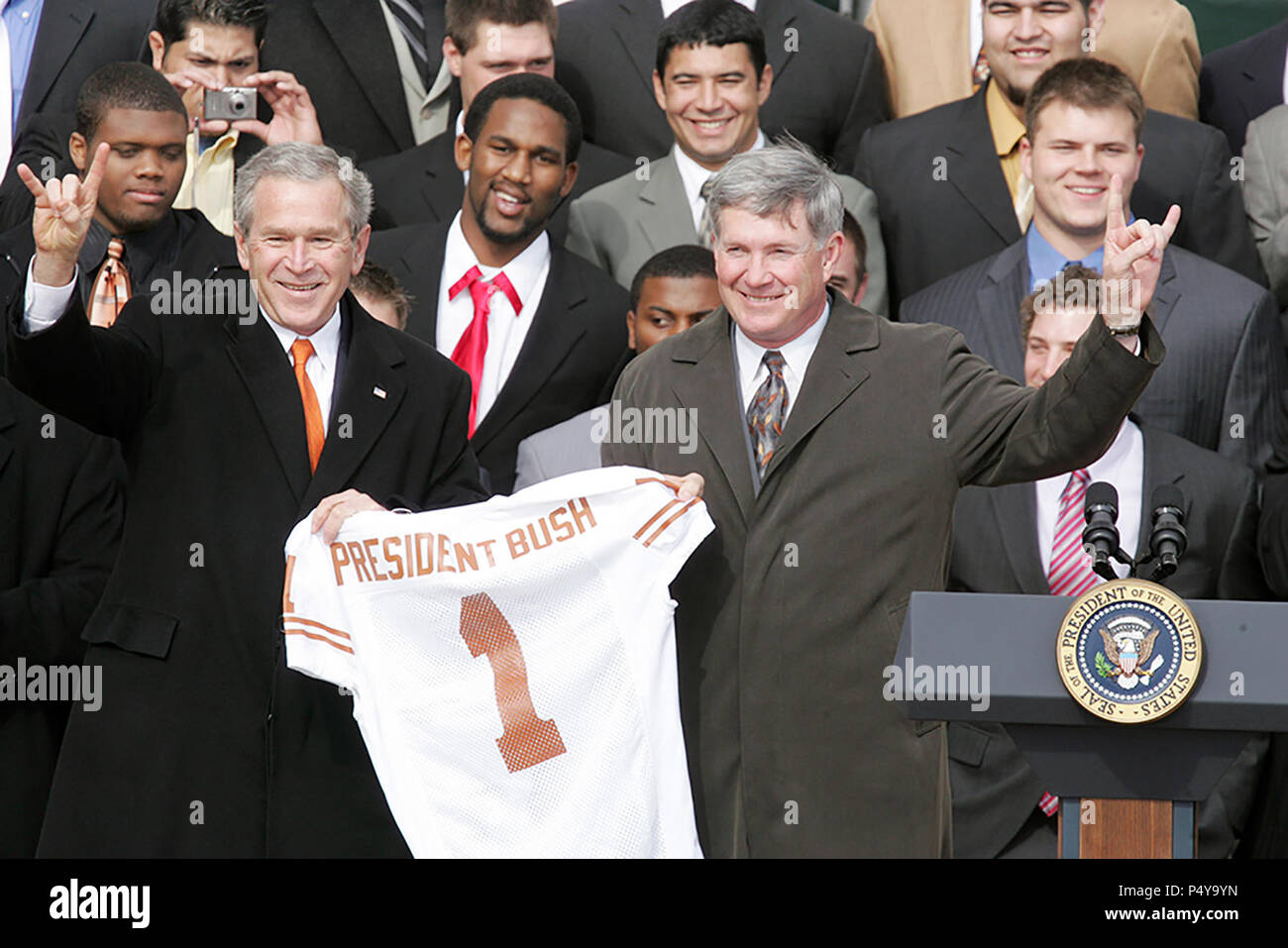 President George W. Bush holds up a University of Texas Longhorns jersey with head football coach Mack Brown, as they give the 'Hook Em Horns' sign, Tuesday, Feb. 14, 2006 on the South Lawn of the White House, during ceremonies to honor the 2005 NCAA Football Champions. Stock Photo
