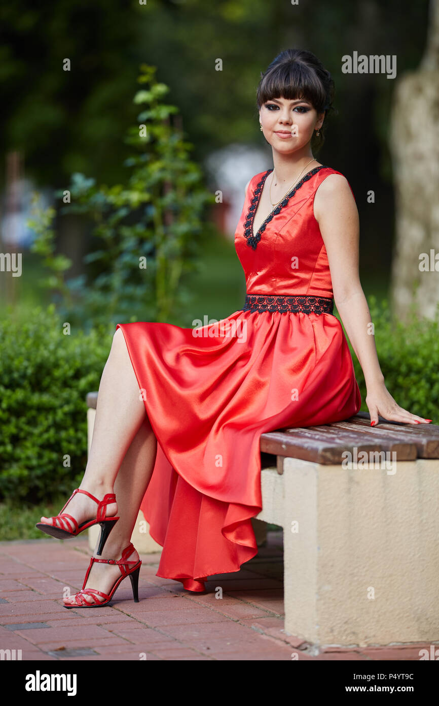 Attractive young girl in red dress sitting on a bench in the park Stock ...