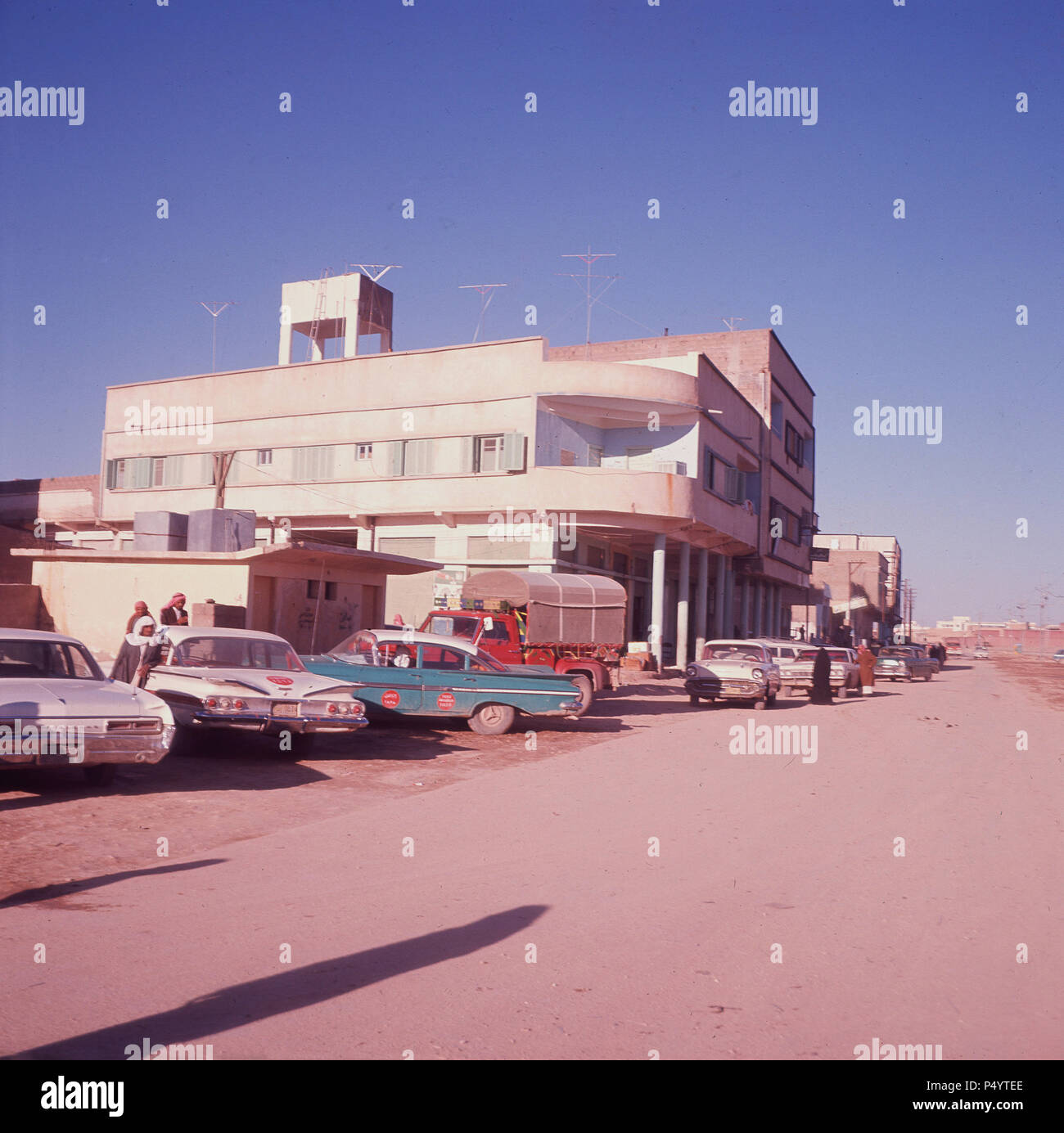 Mid-1960s, historical, Saudi Arabia, American cars parked outside a building at Al-Kharj, known as the Al Kharj oasis, because of the deepwater wells located there. It subsquently grew to become the agriculture production centre of Saudi Arabia after the first experimental farm was established there in 1938. in the 1950s and 60s, the Arabian-American Oil Co, (ARAMCO) had responsibility for the Al Kharj farms which produced food for King Abdul and the Saudi Royal household.and the area became to look 'a little like west Texas'. Stock Photo