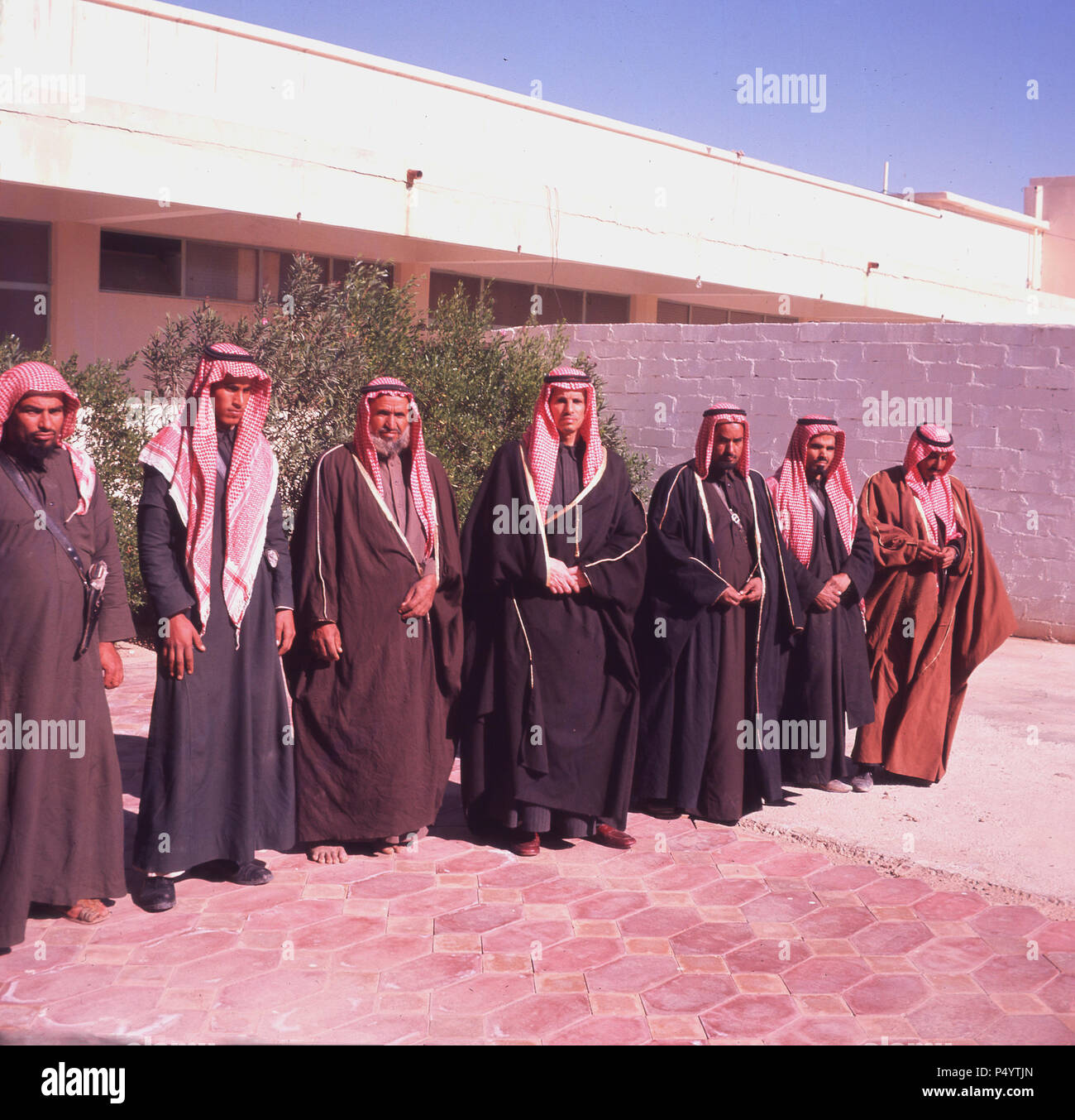 1960s, historical, at the Al-Kharj oasis, the Saudi Prince of Kharj standing outside a building with his advisors, Saudi Arabia. The men are all dressed in thawbs, the ankle-length garments that are traditional cothing for arabian males. Al-Kharj is situated by a number of deepwater pools and an experimental farm was established there in 1938. The following years saw the area became an important place for the development of Saudi agriculture. Stock Photo