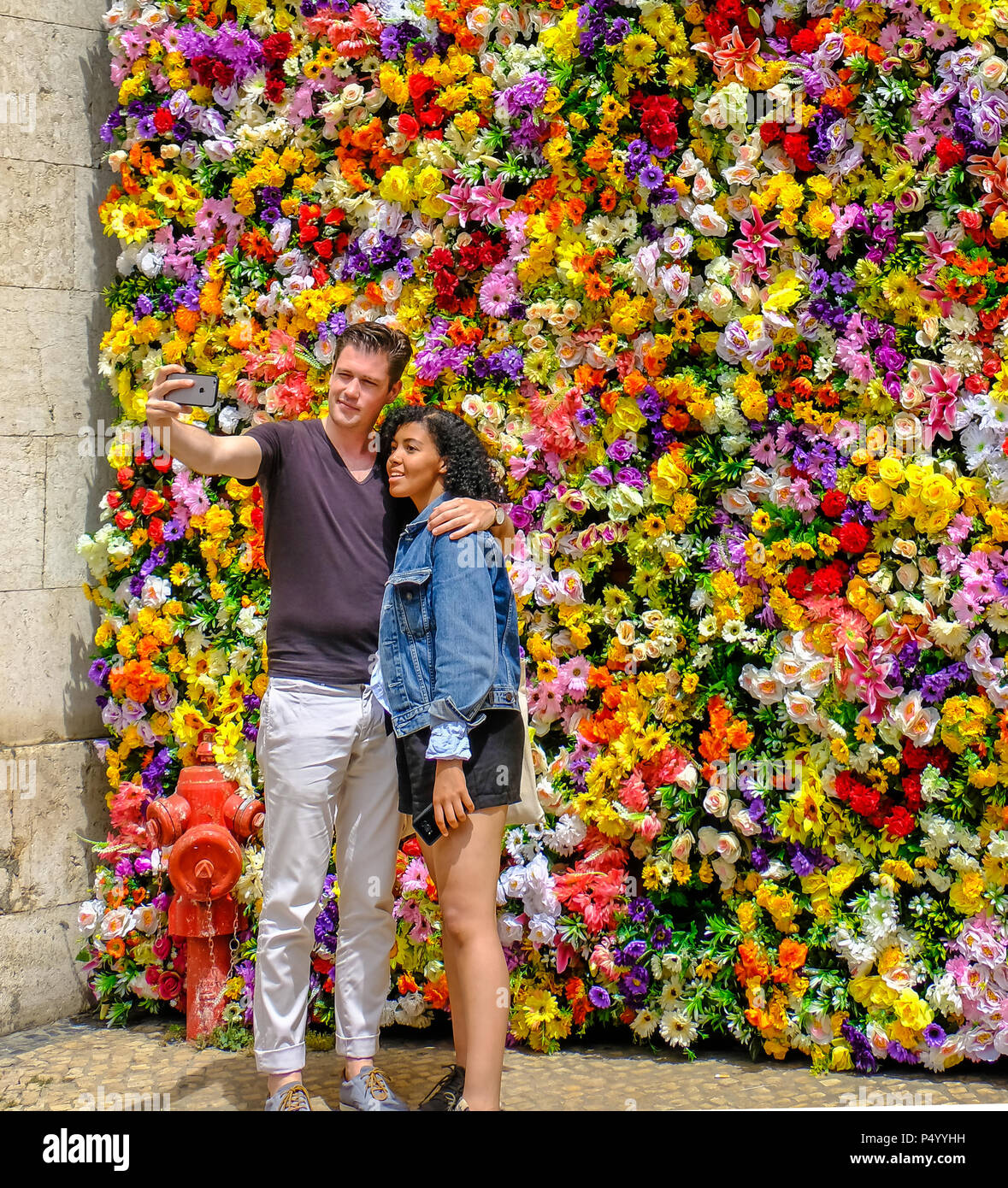 Young white man and beautiful black woman taking selfies before the colorful flowery wall Stock Photo