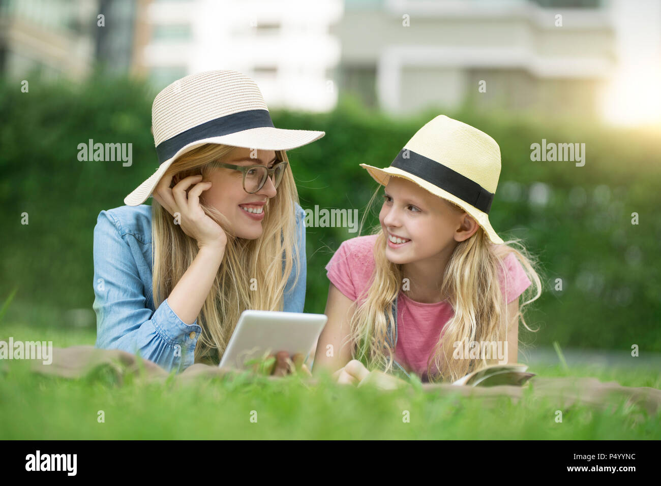Happy mother and daughter with book and smartphone in urban city garden Stock Photo