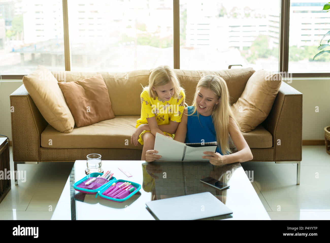 Happy mother and daughter sitting on a couch looking at the girl's homework together Stock Photo