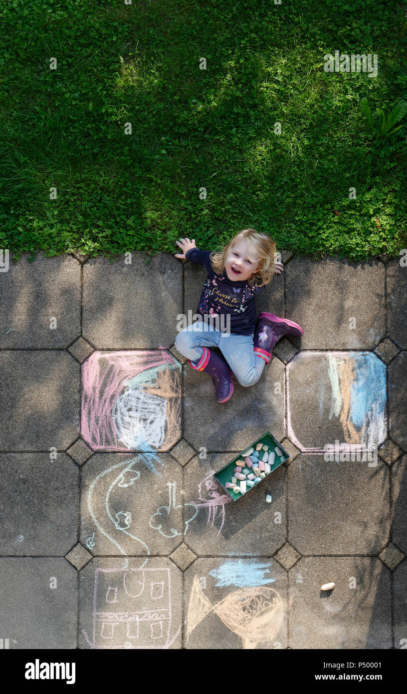 Smiling little girl drawing with chalk outdoors, top view Stock Photo