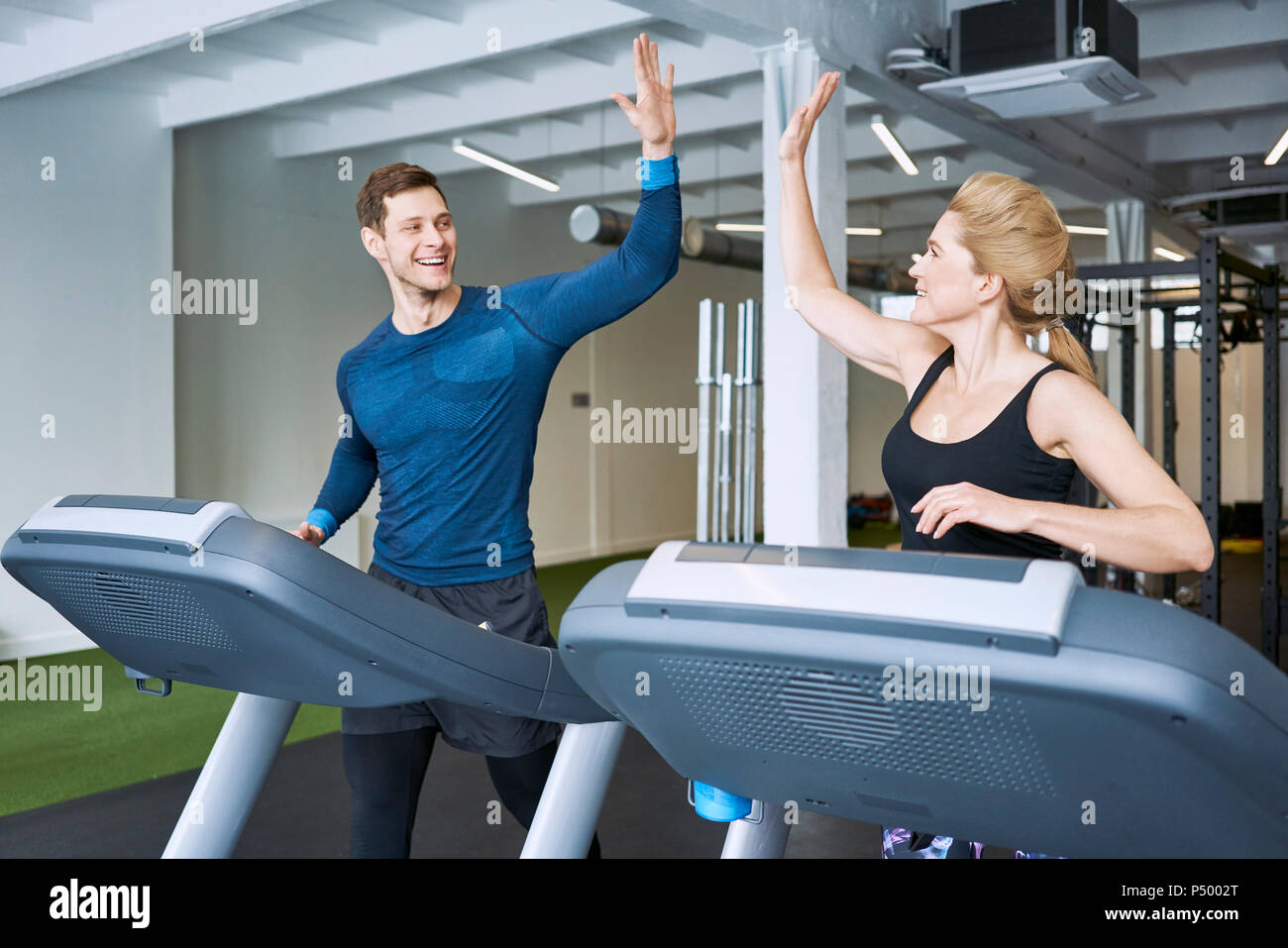 Happy man and woman doing high five during treadmill exercise at gym Stock Photo