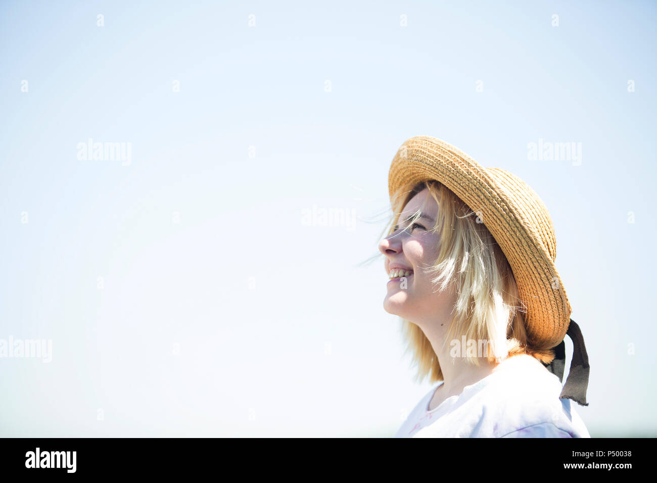Young smiling woman with sun hat looking up, blue sky, copy space Stock Photo