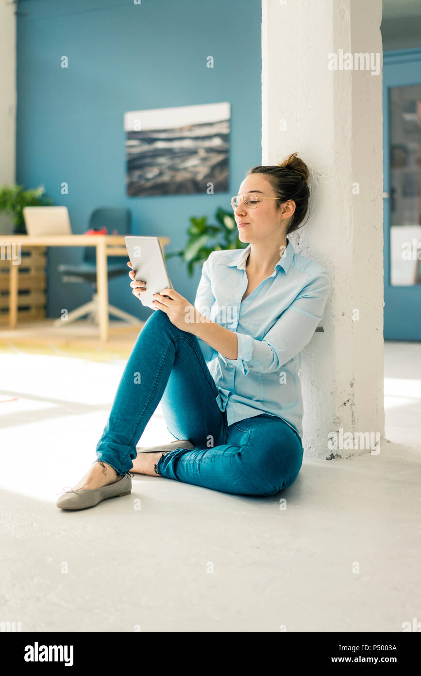 Young freelancer sitting on the floor in her studio using tablet Stock Photo