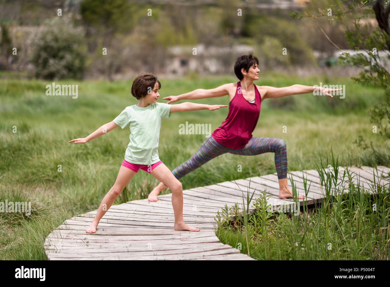 Mother and daughter doing yoga on boardwalk Stock Photo