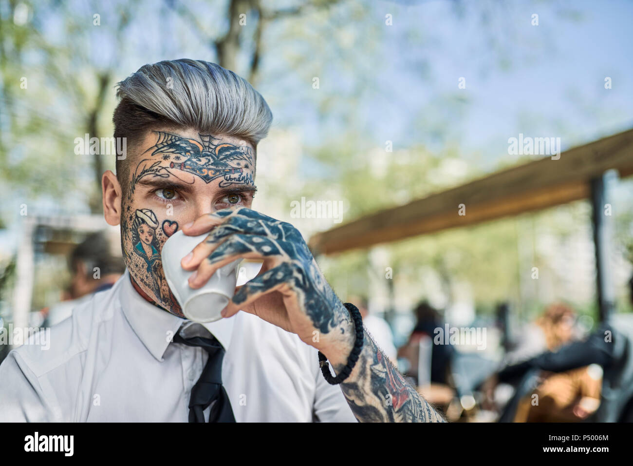 Young businessman with tattooed face, drinking coffee Stock Photo