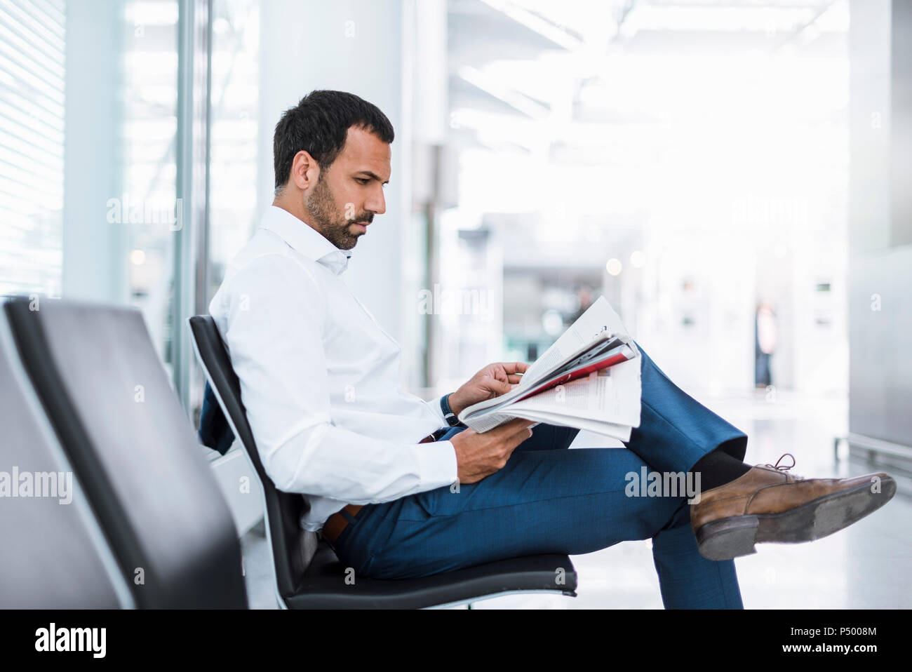 Businessman reading a newspaper in waiting hall Stock Photo