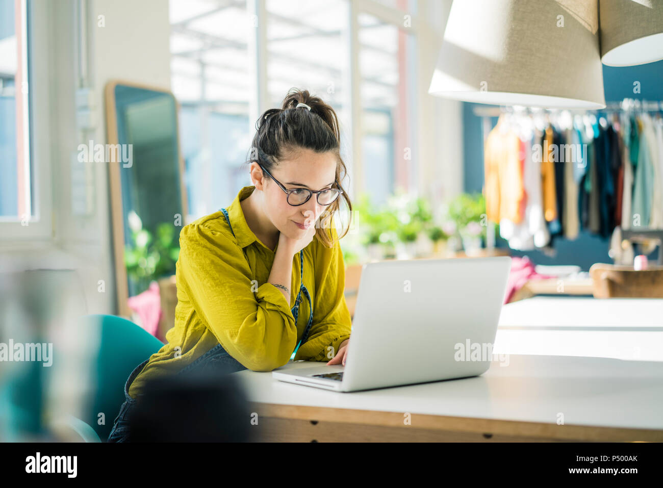 Fashion designer sitting at desk in her studio looking at laptop Stock Photo