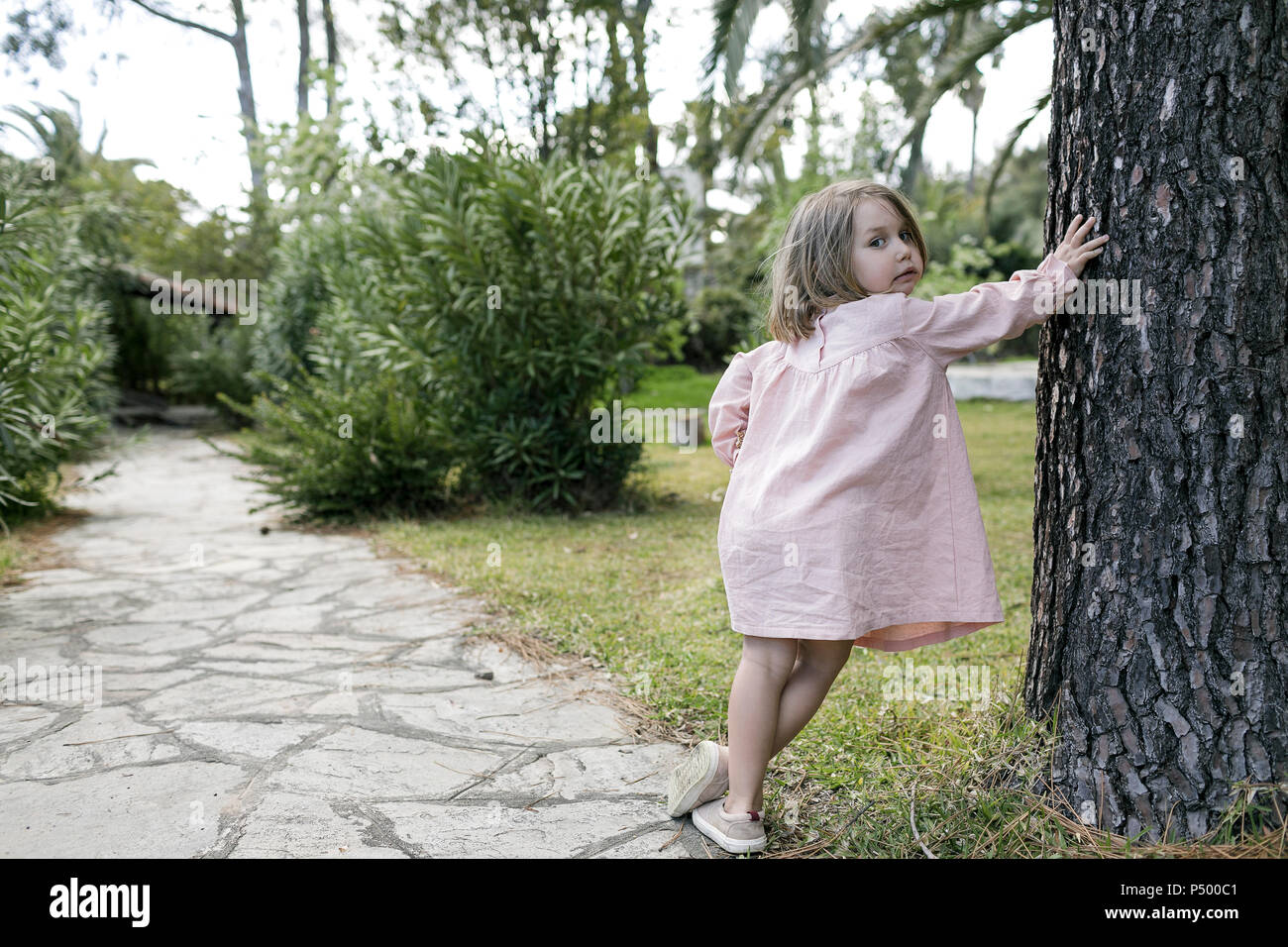 Portrait of little girl leaning against tree trunk in garden Stock Photo
