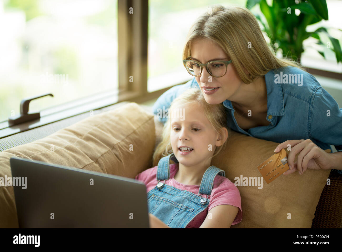 Mother and daughter in modern living room on a couch with laptop and credit card Stock Photo