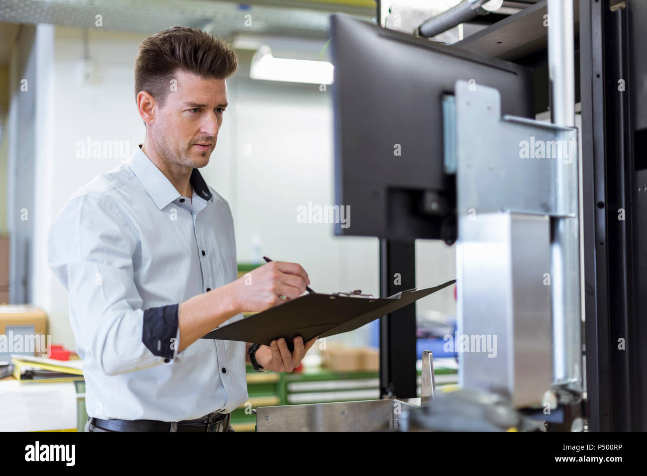 Man with clipboard in factory looking at screen Stock Photo