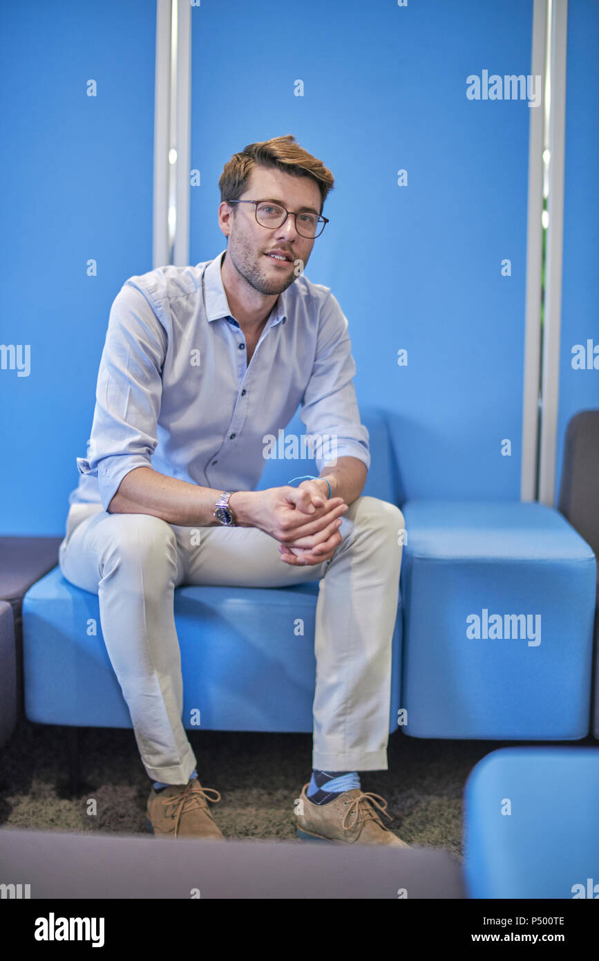 Portrait of businessman sitting on light blue stool in an office Stock