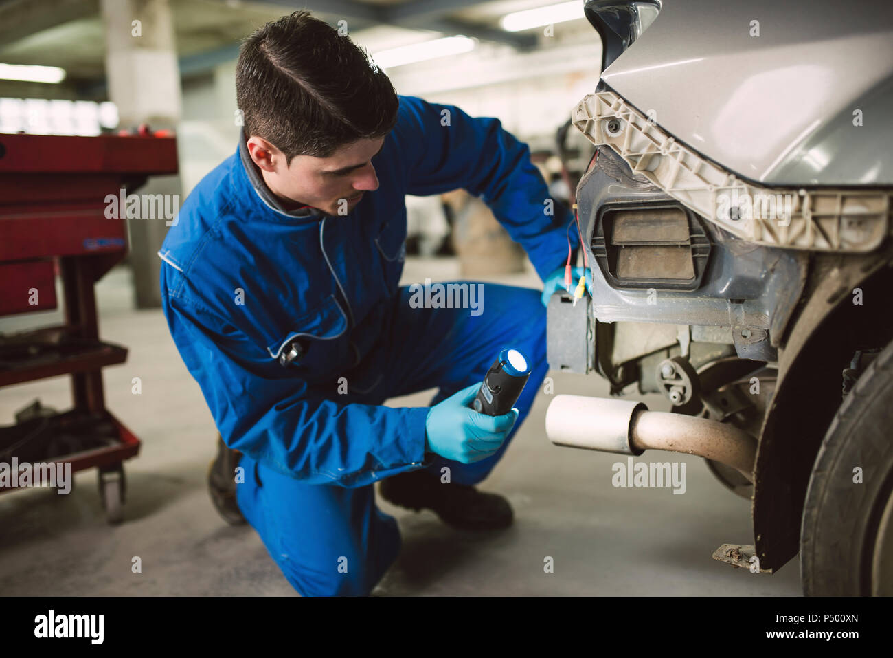 Mechanic inspecting a car with a torch in a workshop Stock Photo