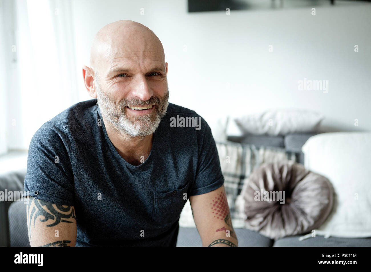 Tattooed man at home sitting on couch Stock Photo