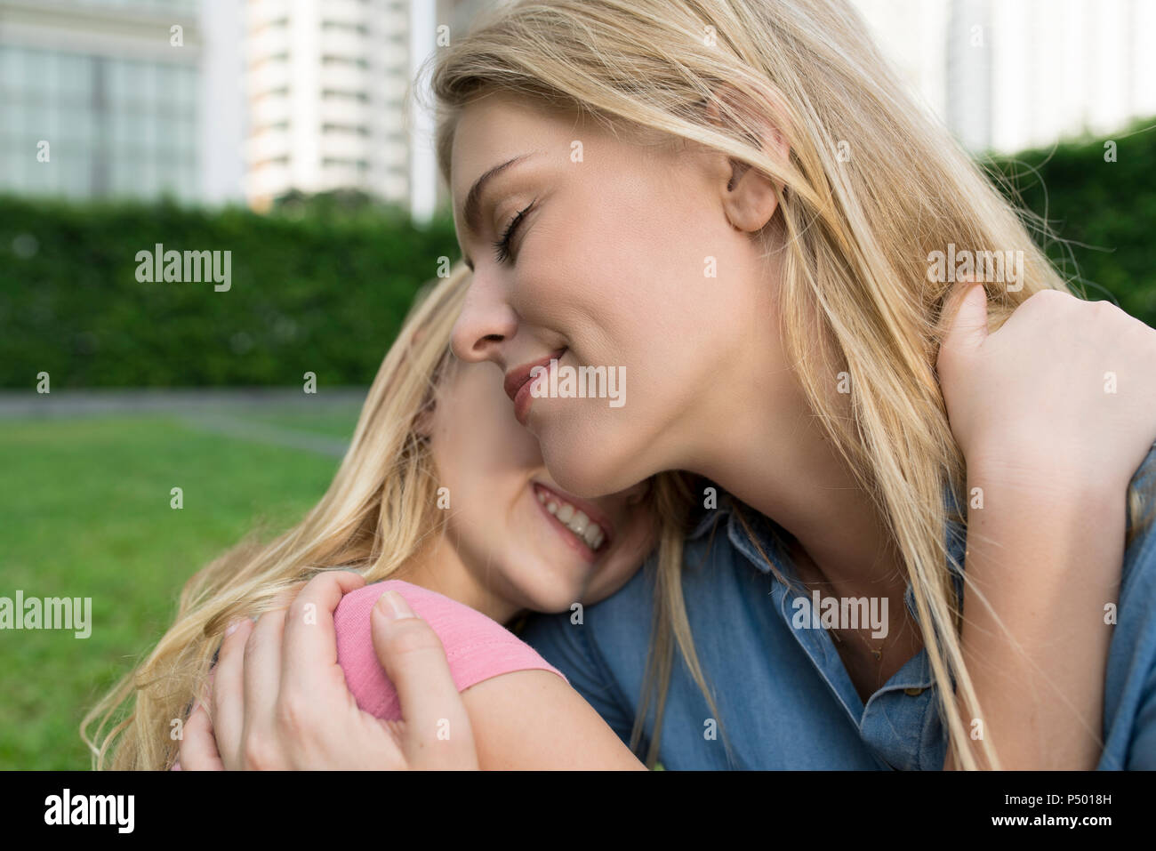 Happy mother and daughter hugging and smiling in urban city garden Stock Photo