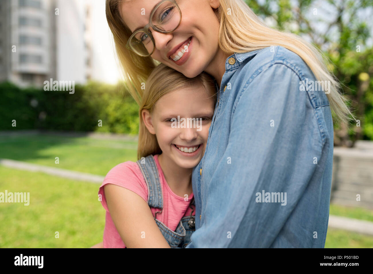 Happy mother and daughter hugging and smiling in urban city garden Stock Photo