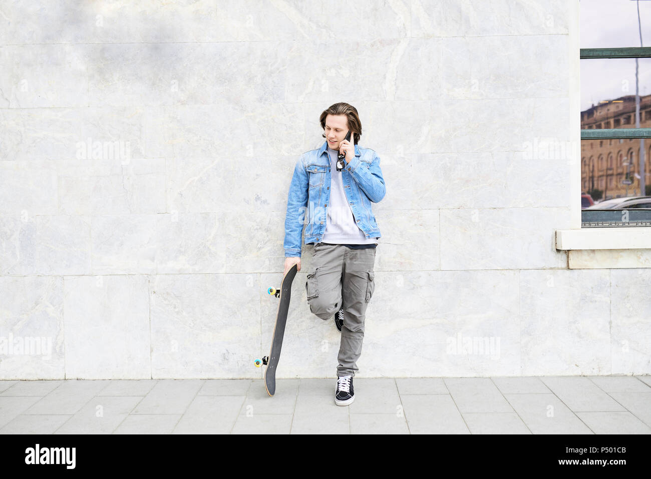 Young man holding skateboard, using smartphone Stock Photo