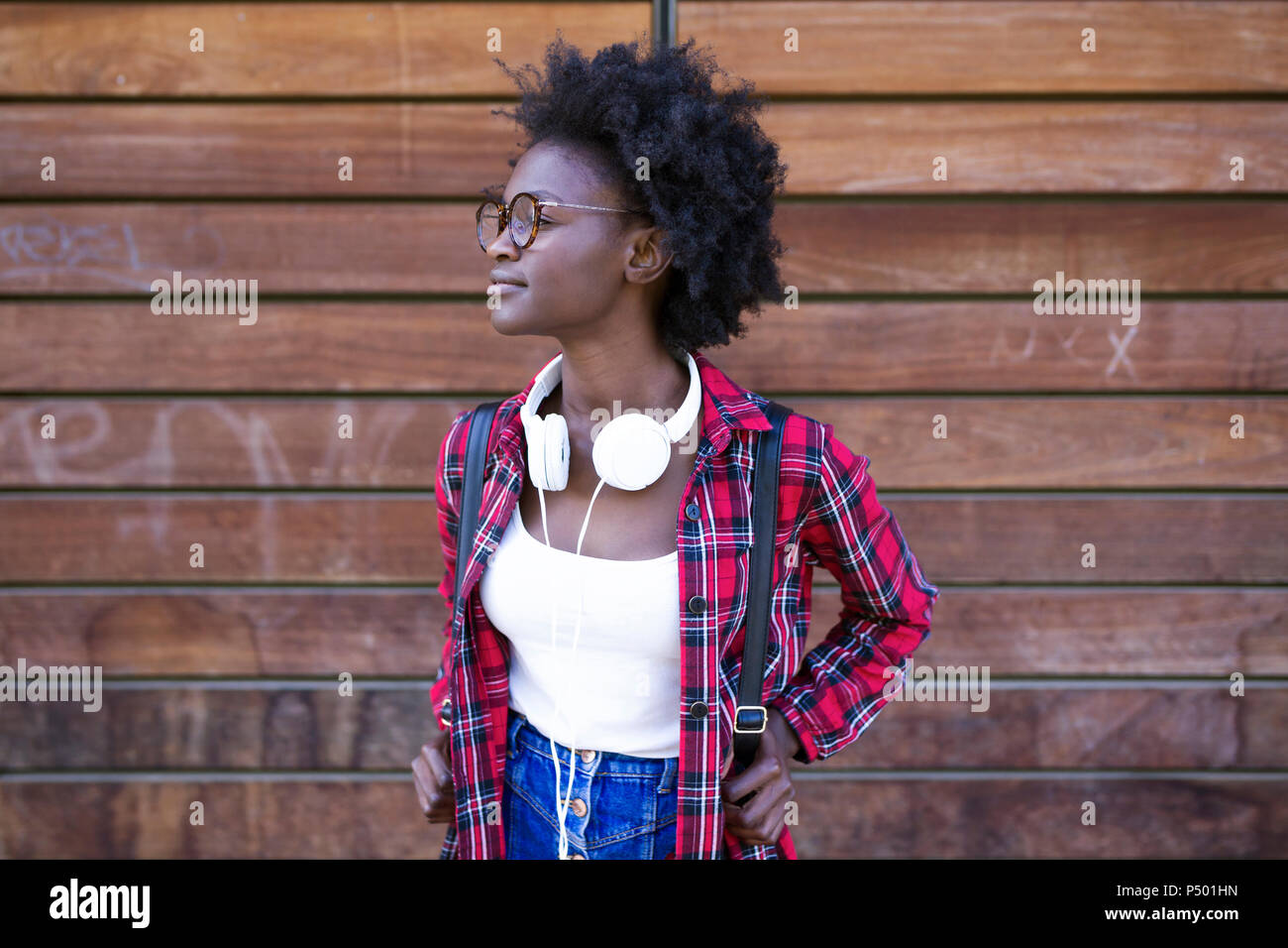 Young woman with backpack and headphones waiting in front of wooden wall Stock Photo