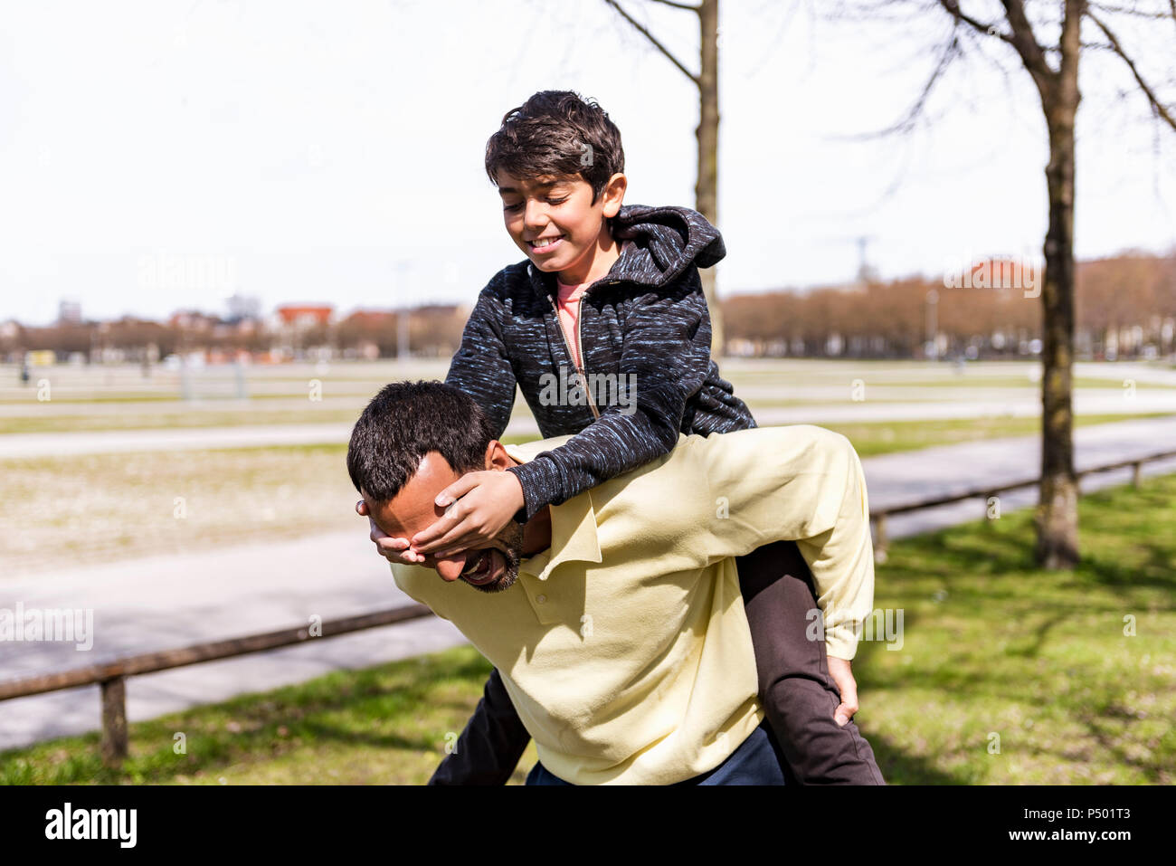 Happy father carrying son piggyback in a park Stock Photo