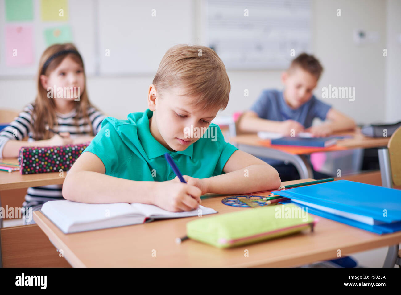 Schoolboy writing in exercise book in class Stock Photo