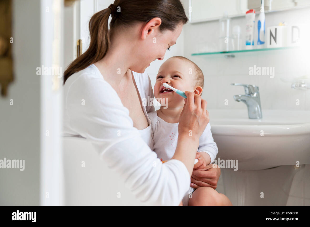 Mother brushing baby's teeth in bathroom Stock Photo