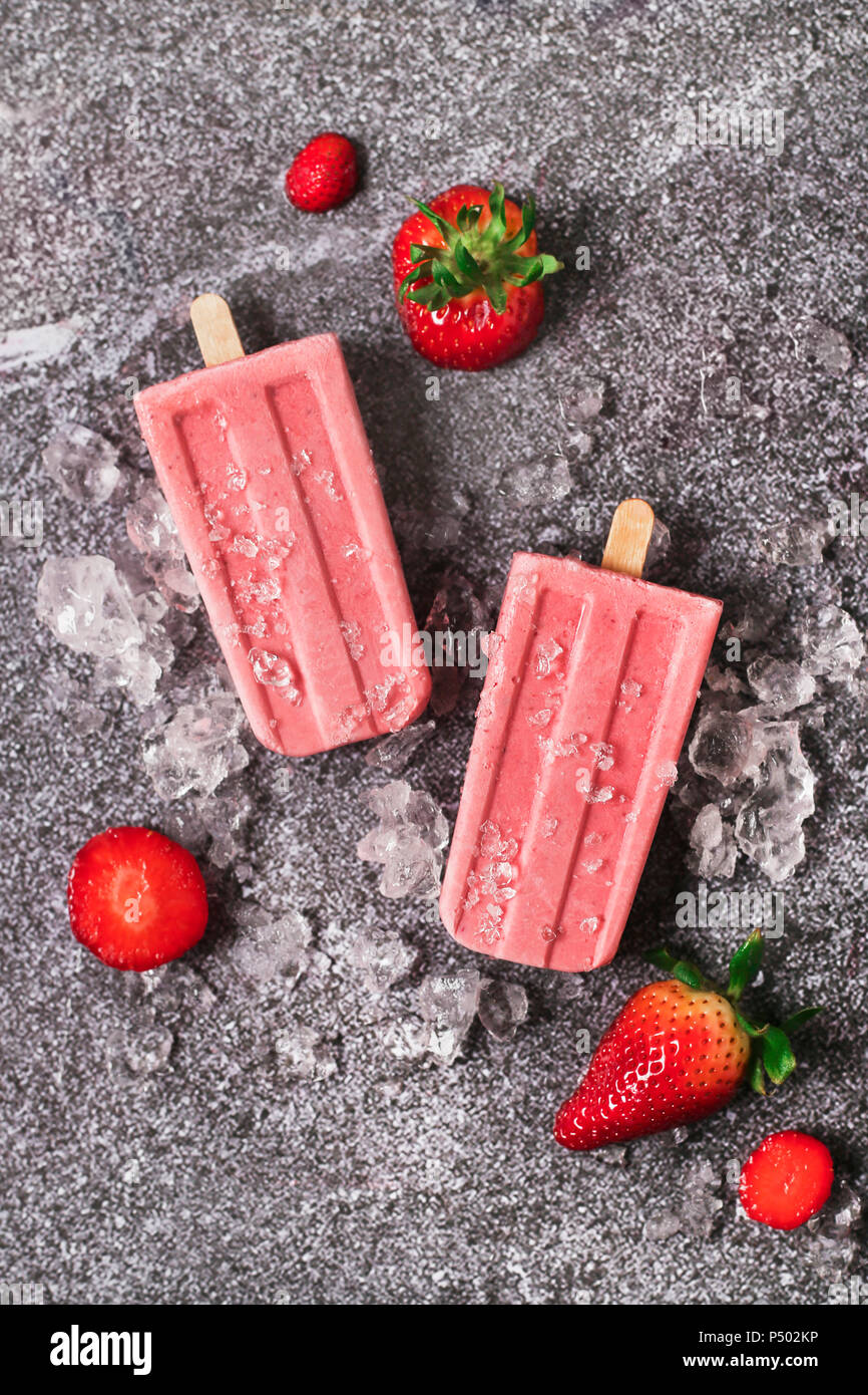 Two homemade strawberry ice lollies, ice and strawberries on marble Stock Photo