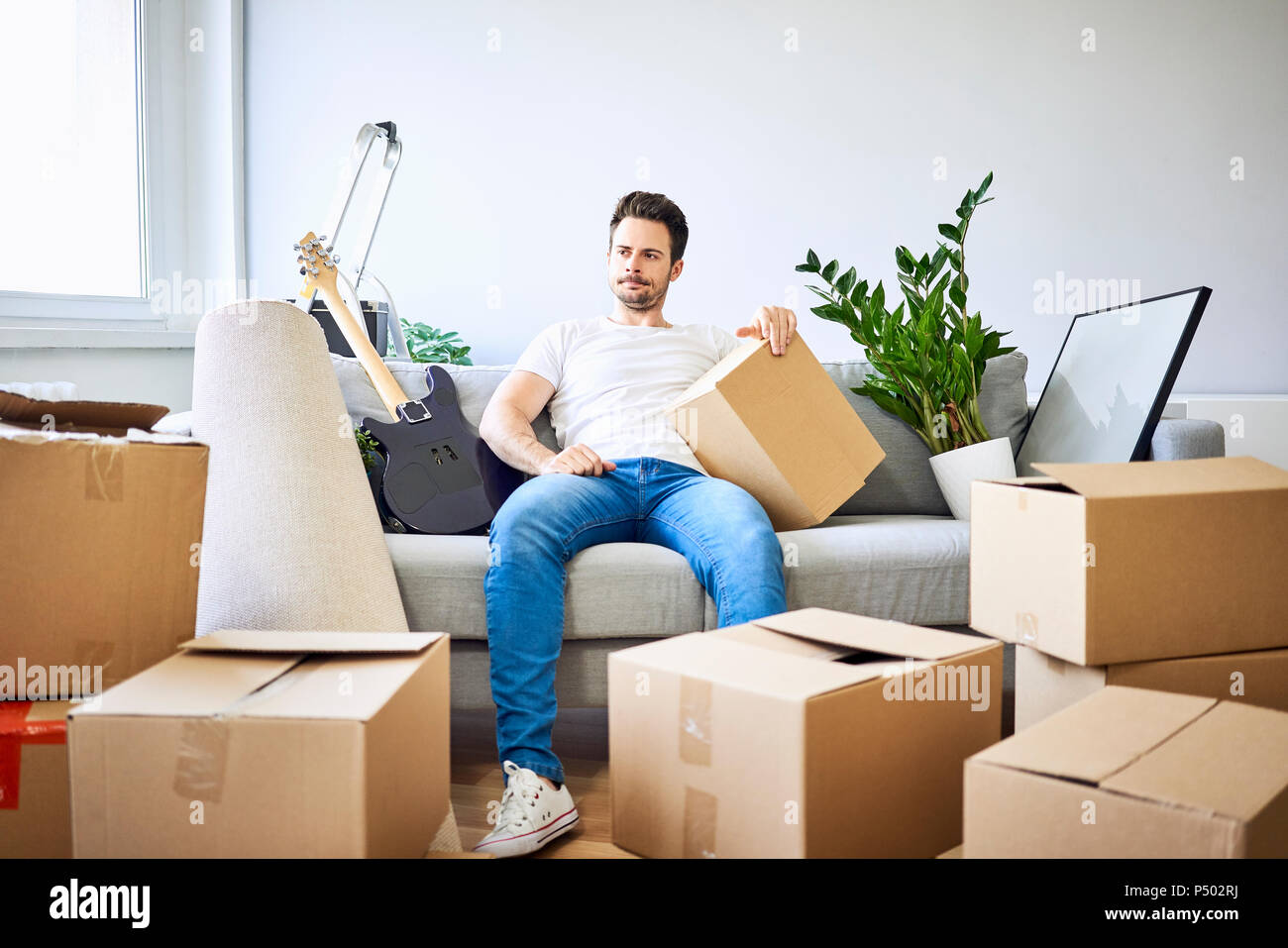 Frustrated man sitting on couch surrounded by cardboard boxes Stock Photo