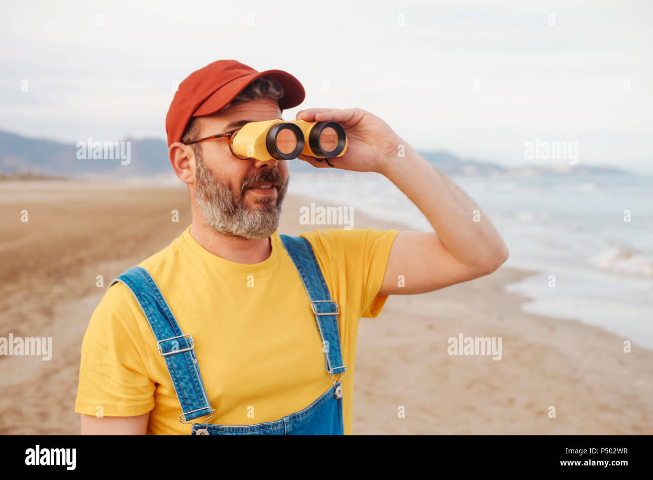 Bearded man using binoculars on the beach Stock Photo