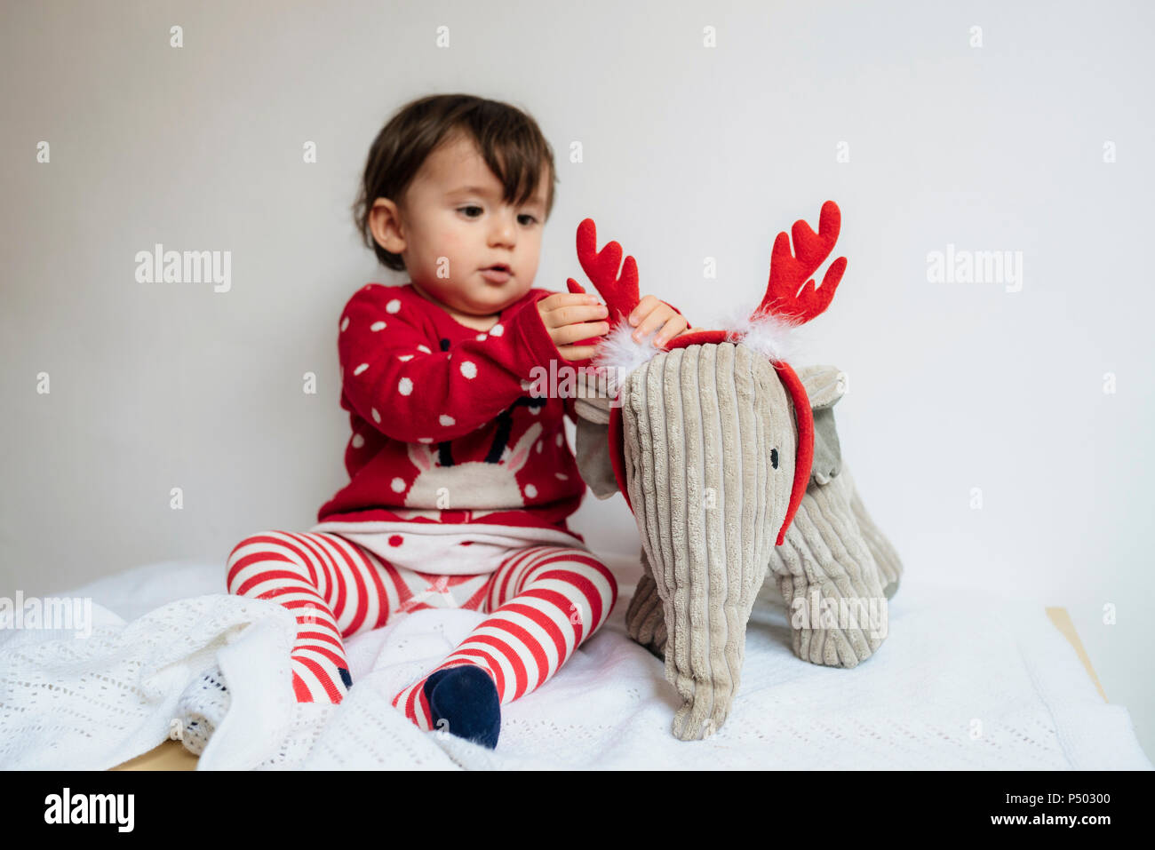 Baby girl playing with reindeer antlers headband and toy elephant Stock Photo