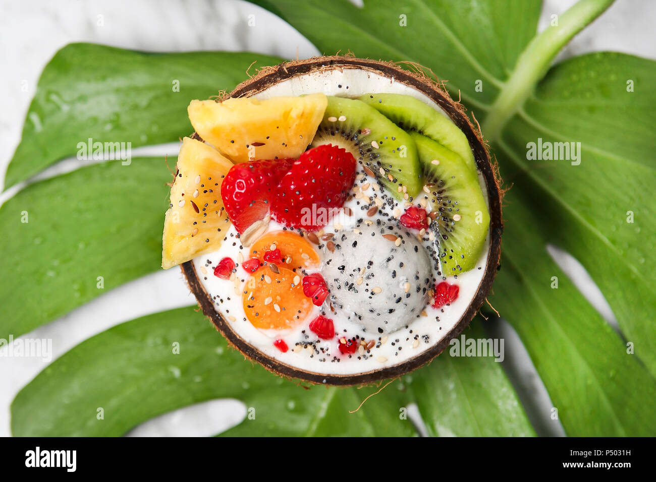 Coconut bowl with variuos fruits, natural yoghurt and seeds on leaf Stock Photo