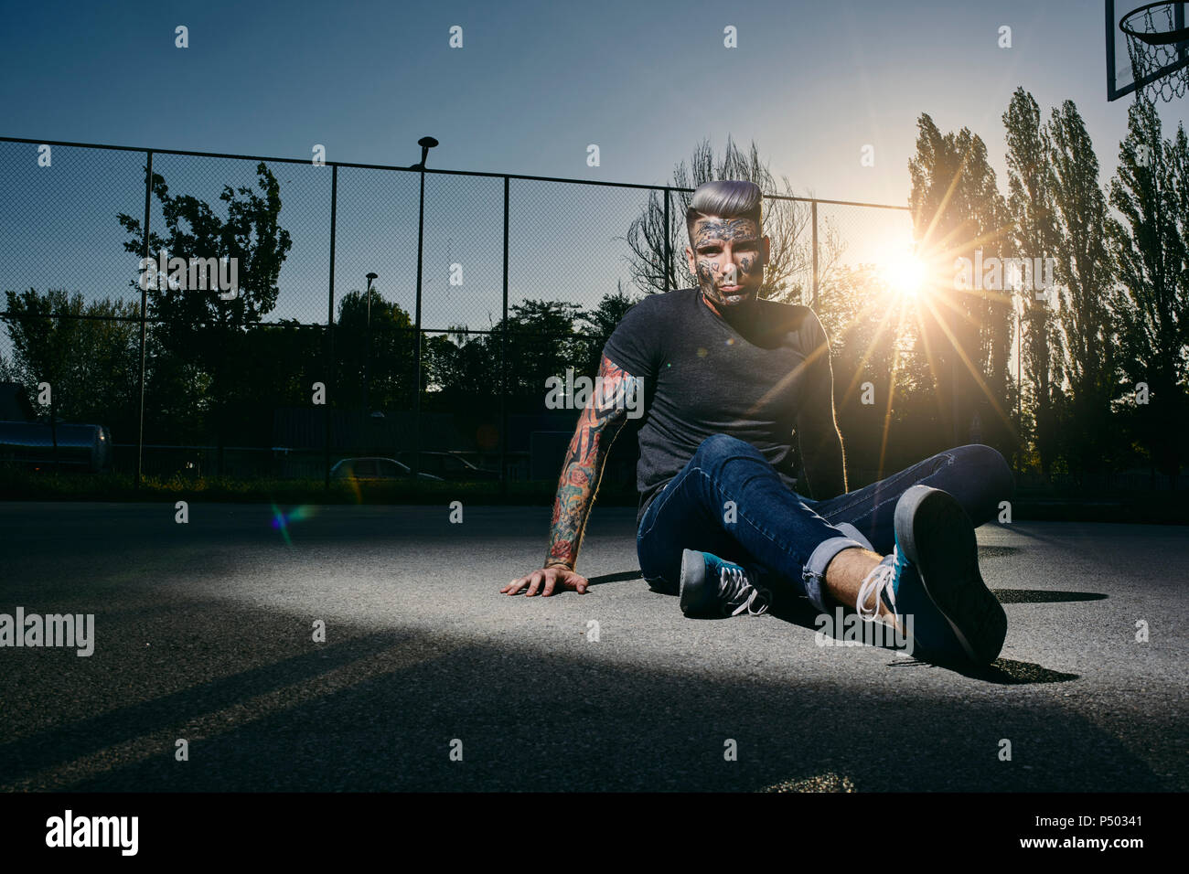 Portrait of tattooed young man sitting on basketball court at sunset Stock Photo