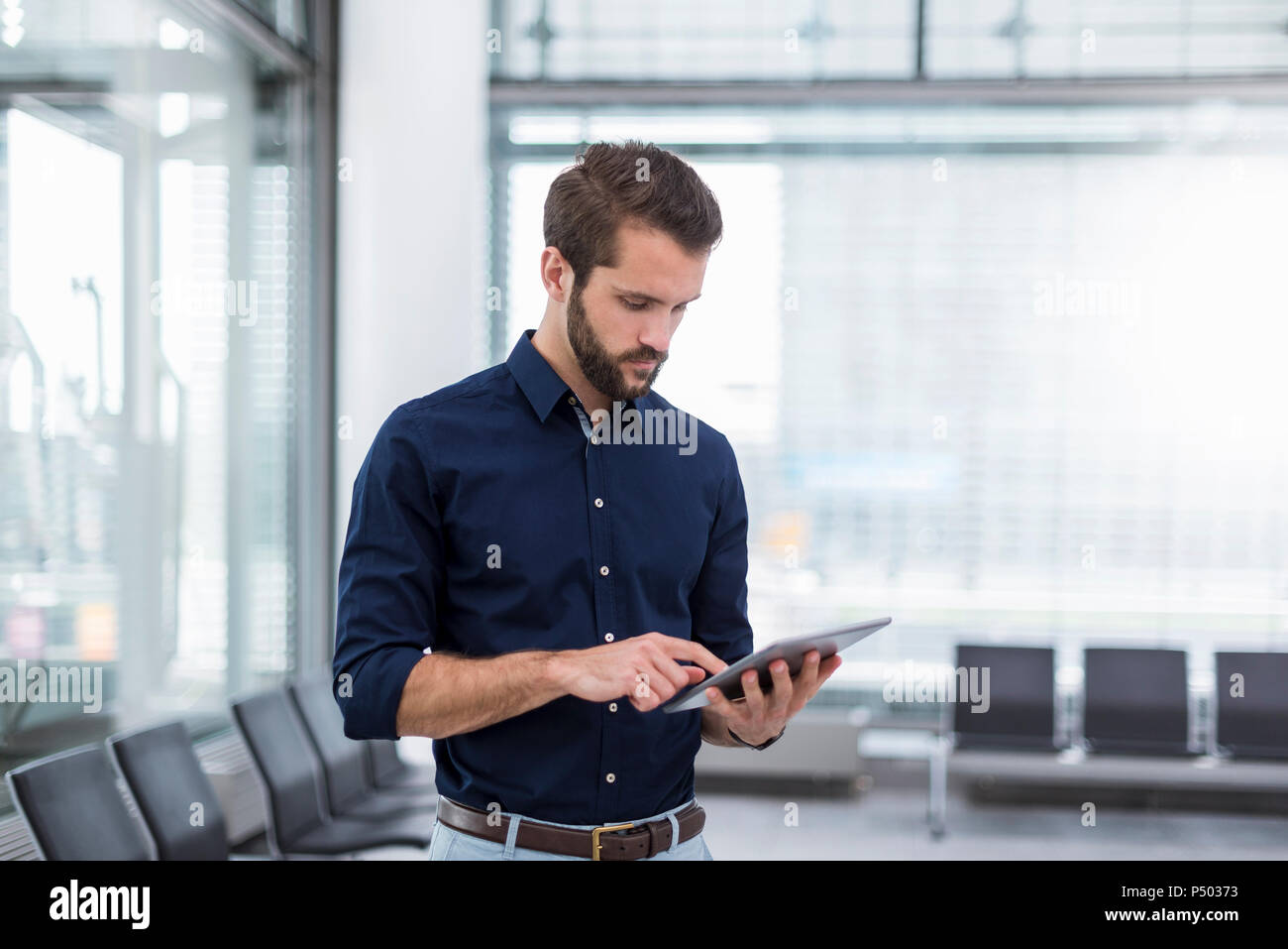 Young businessman standing in waiting area using tablet Stock Photo