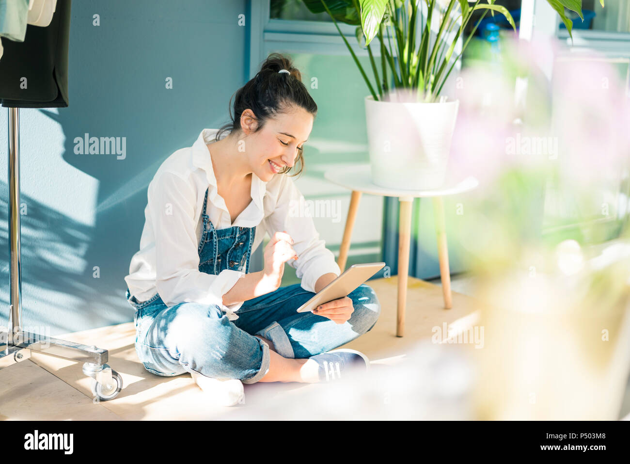 Smiling young freelancer sitting on the floor in her studio using tablet Stock Photo