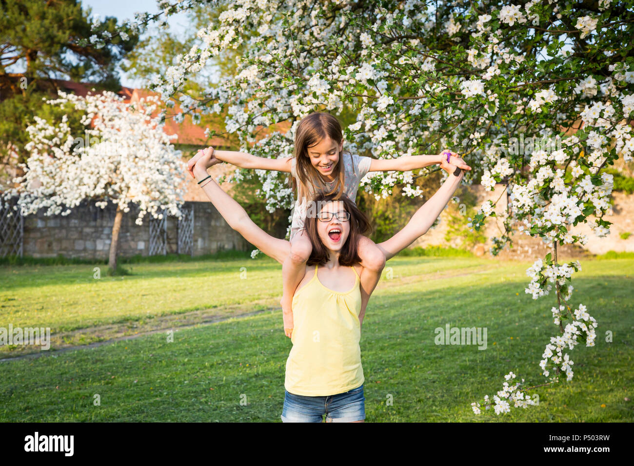 Girl carrying little sister on her shoulders in the garden Stock Photo