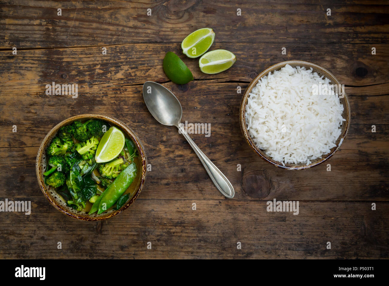 Green thai curry with broccoli, pak choi, snow peas, baby spinach, lime and bowl of rice Stock Photo