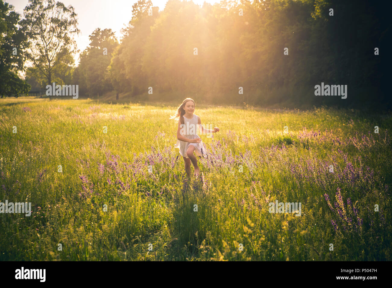 Smiling girl running on flower meadow at evening twilight Stock Photo