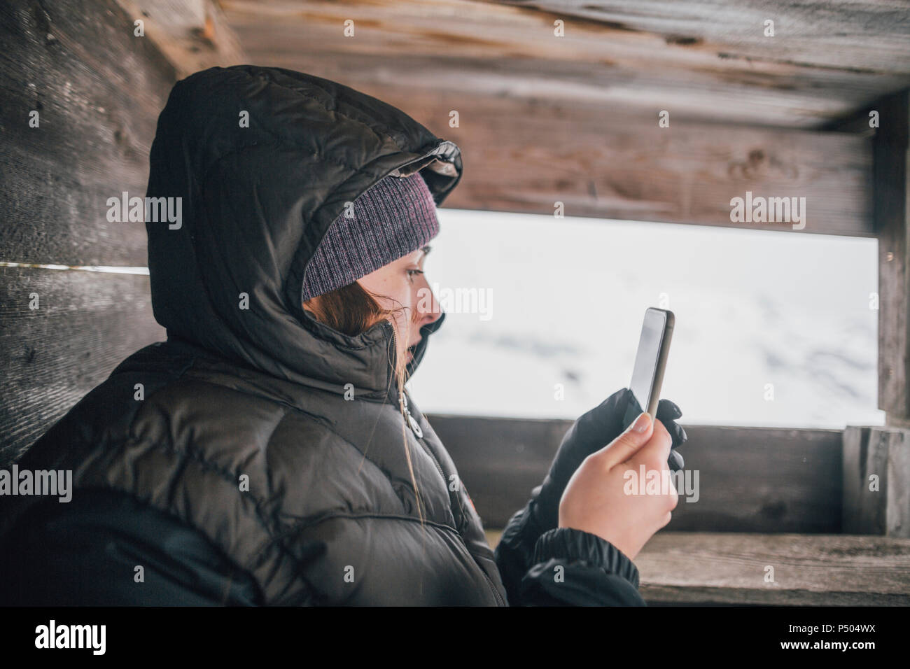 Austria, Kitzbuehel, young woman in raised hide looking at cell phone in winter Stock Photo
