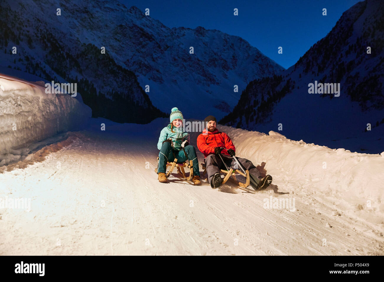 Couple sledding in snow-covered landscape at night Stock Photo