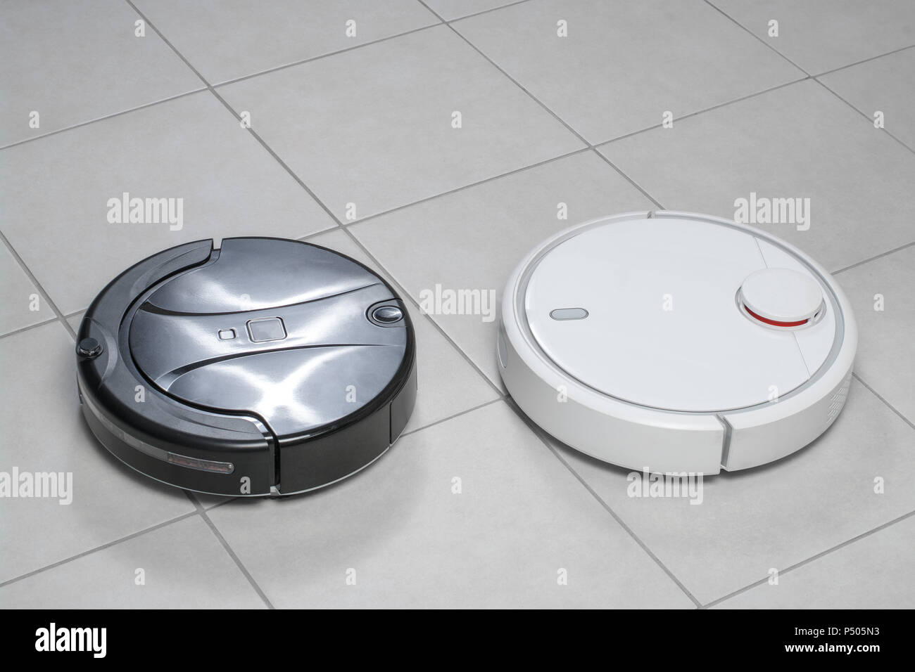 Two different robotic vacuum cleaners models cleaning dust on tile