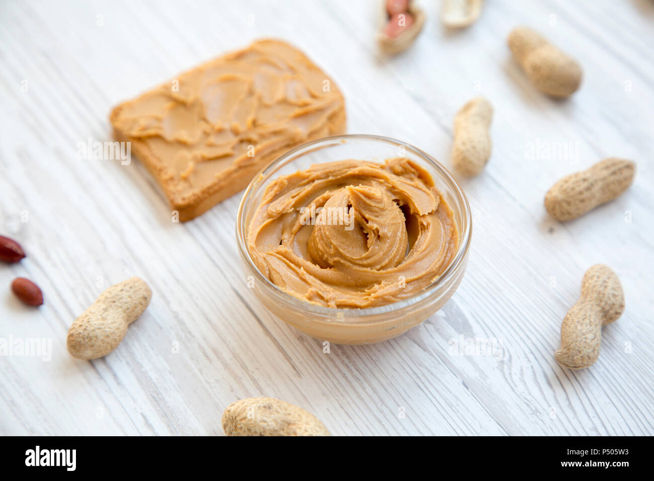 Toast, bowl of peanut butter and peanuts in shells on a white wooden background, side view. Stock Photo