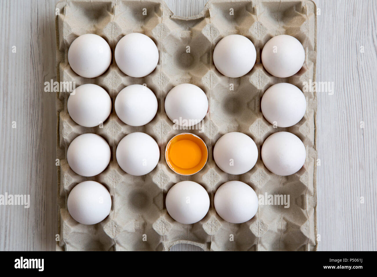 Cracked egg among other chicken eggs in carton egg box, top view. From
